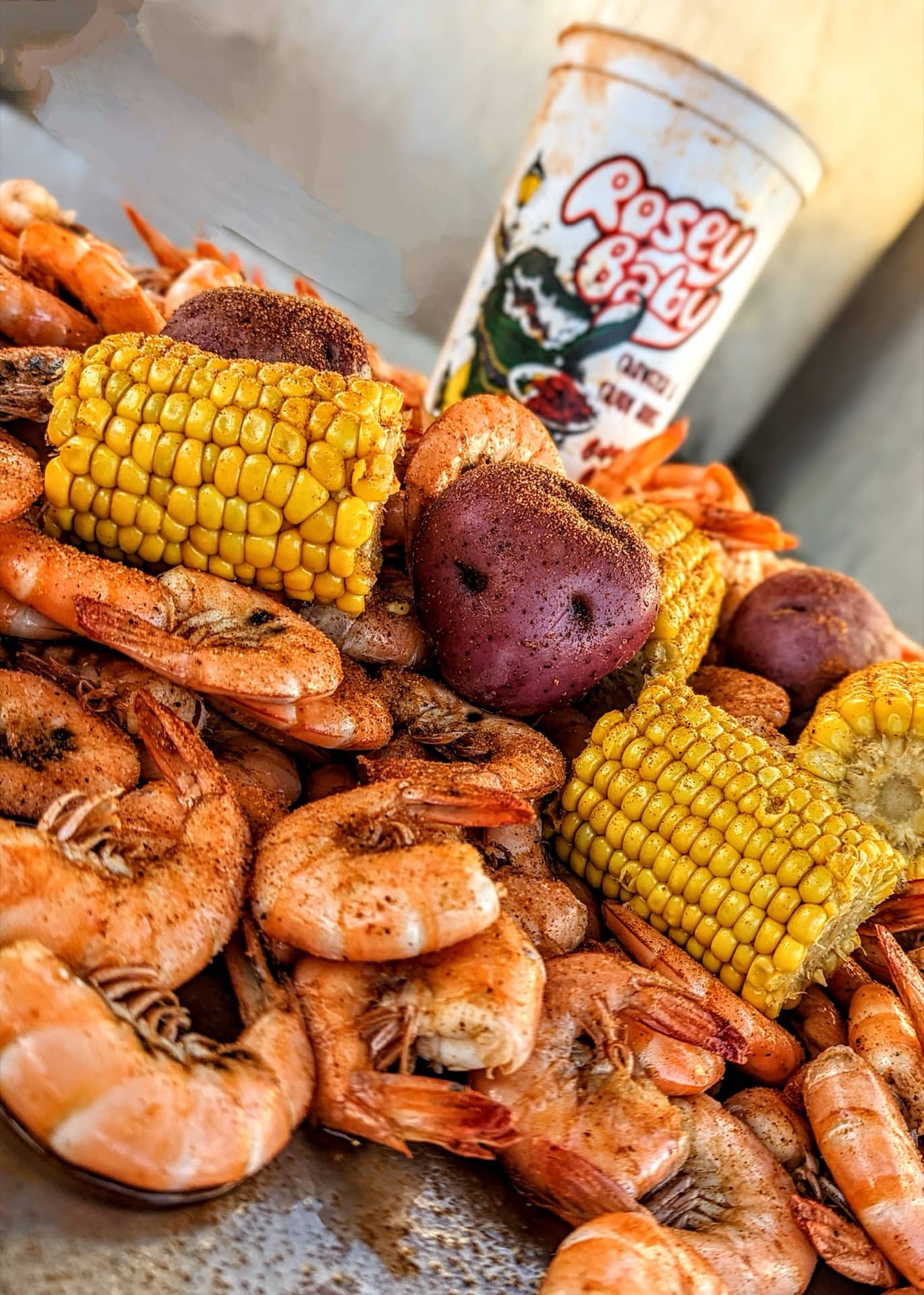 Boiled shrimp, corn, and potatoes with a branded Rosey Baby cup